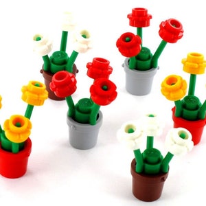 Puede incluir: Una colección de coloridos arreglos florales de juguete. Cada arreglo presenta flores rojas, amarillas y blancas, con tallos y hojas verdes, plantadas en pequeñas macetas de varios colores, incluyendo rojo, marrón y gris. Las flores son de plástico.