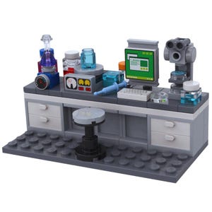 Może przedstawiać: Plastikowy zestaw laboratoryjny w kolorze szarym i białym z komputerem, mikroskopem, zlewami i taboretem. Zestaw zawiera różne akcesoria, takie jak probówki, kolby i szalki Petriego.