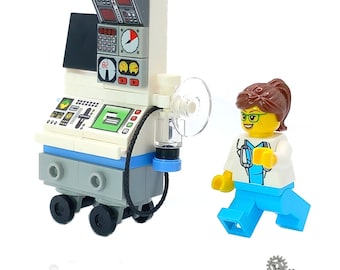 May include: A white LEGO® medical equipment model with a blue base and black wheels. The model has a monitor with a digital display and a stethoscope. A LEGO® minifigure of a doctor with brown hair, a white coat, and a stethoscope is standing next to the equipment. The image includes the text "LEGO®" and "HOSPITAL".