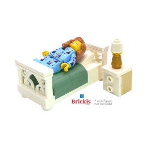 Op de afbeelding: Een wit LEGO-bed met een groen dekbed en een wit LEGO-nachtkastje met een lamp. Het bed heeft een decoratief hoofdeinde en voeteneinde.  *Minifigure niet inbegrepen*
