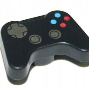 Könnte beinhalten: Ein schwarzer Kunststoff-Videospiel-Controller mit einem Steuerkreuz, zwei grauen Knöpfen und vier farbigen Knöpfen: blau, rot, blau und rot. Der Controller ist einteilig und hat eine abgerundete Form.