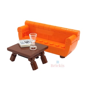 Peut inclure: Canapé orange en Lego avec une table basse en Lego marron et un verre en Lego transparent. La table basse a un petit journal sur le dessus.