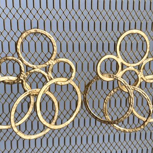 Può includere: Un paio di orecchini dorati con un gruppo di cerchi sovrapposti. Gli orecchini sono in metallo e hanno una texture martellata.