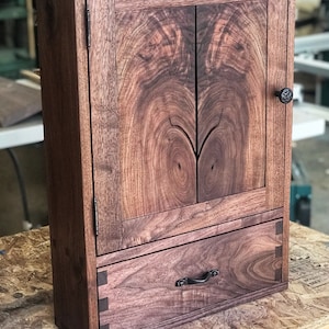 May include: A dark brown wooden cabinet with a single drawer and two doors. The cabinet has a natural wood finish and is made of walnut wood. The cabinet has a simple design with a single drawer and two doors. The cabinet is made of solid wood and has a natural wood finish.