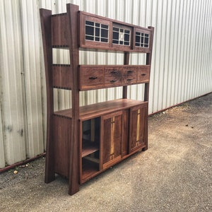 K&ouml;nnte beinhalten: Ein hoher, brauner Holzschrank. Der Schrank hat mehrere Regale, Schubladen und T&uuml;ren. Die T&uuml;ren sind aus Holz mit einer hellbraunen Maserung. Der Schrank steht auf einer Betonfl&auml;che.