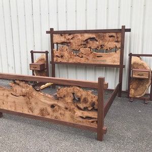 May include: A wooden bed frame with a unique headboard and footboard made from a single piece of wood with natural burls and knots. The bed frame is dark brown and has a simple, modern design. Two matching nightstands with drawers are included.