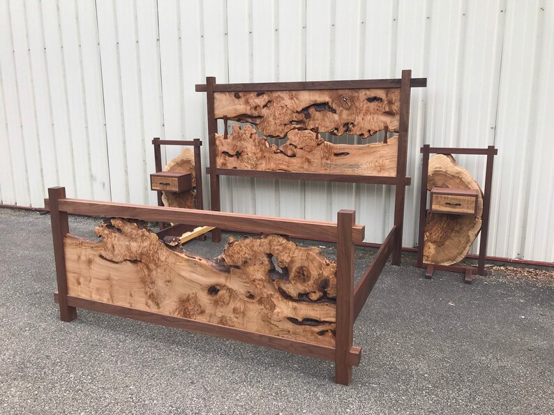 May include: A wooden bed frame with a unique headboard and footboard made from a single piece of wood with natural burls and knots. The bed frame is dark brown and has a simple, modern design. Two matching nightstands with drawers are included.