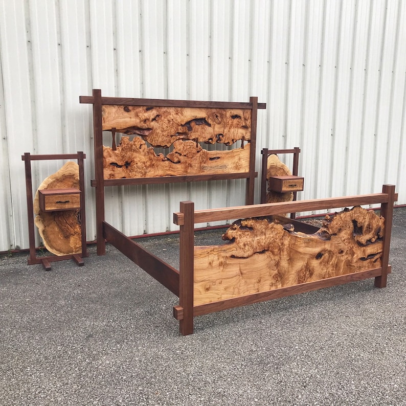 May include: A wooden bed frame with a unique headboard featuring a natural wood grain pattern. The headboard has a cutout design and is supported by two vertical posts. The bed frame is made of dark wood and has a simple, modern design. The bed frame is accompanied by two matching nightstands.
