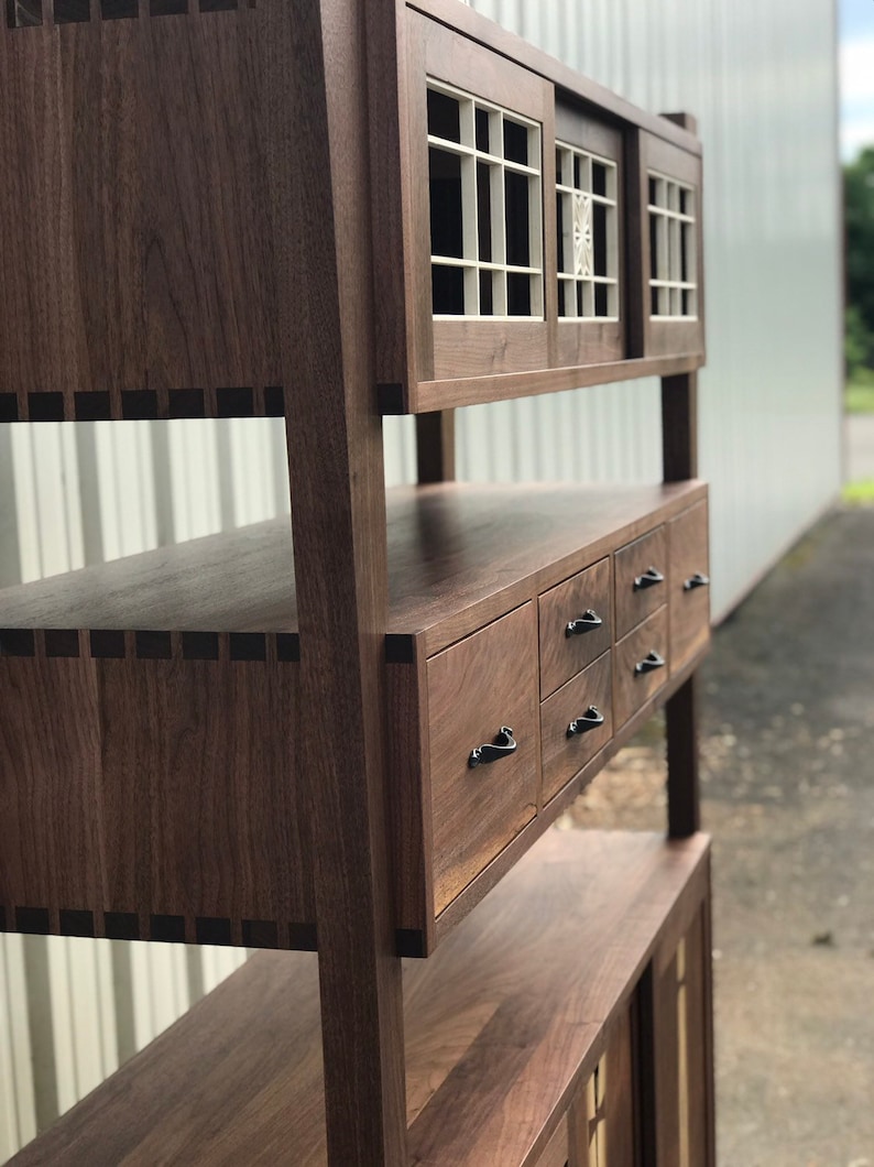 K&ouml;nnte beinhalten: Ein hoher Holzschrank mit dunkelbrauner Oberfl&auml;che. Der Schrank hat zwei Glast&uuml;ren mit einem Gittermuster und eine Reihe von Schubladen darunter. Der Schrank ist aus massivem Holz gefertigt und hat einen traditionellen Stil.