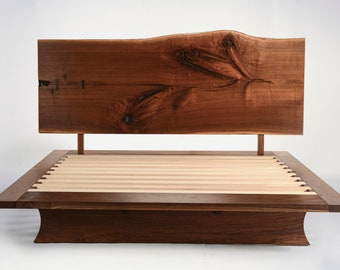 May include: A wooden platform bed frame with a live edge headboard. The headboard is made of dark walnut wood with a natural, organic shape. The platform is made of light wood with a slatted design. The bed frame has a simple, modern design.