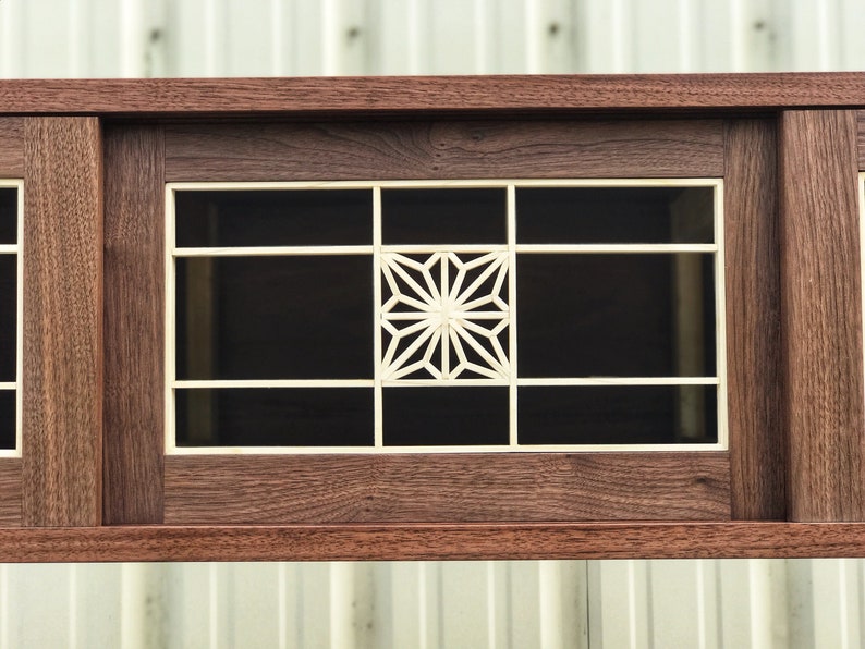 K&ouml;nnte beinhalten: Ein Holzschr&auml;nkchen mit einer Glast&uuml;r, die ein geometrisches Muster in der Mitte zeigt. Der Schrank ist aus dunklem Holz mit einer Einlage aus hellem Holz.