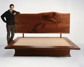 May include: A wooden platform bed frame with a live edge headboard. The headboard is made of a single piece of wood with a natural, organic shape. The bed frame is made of solid wood and has a simple, modern design.