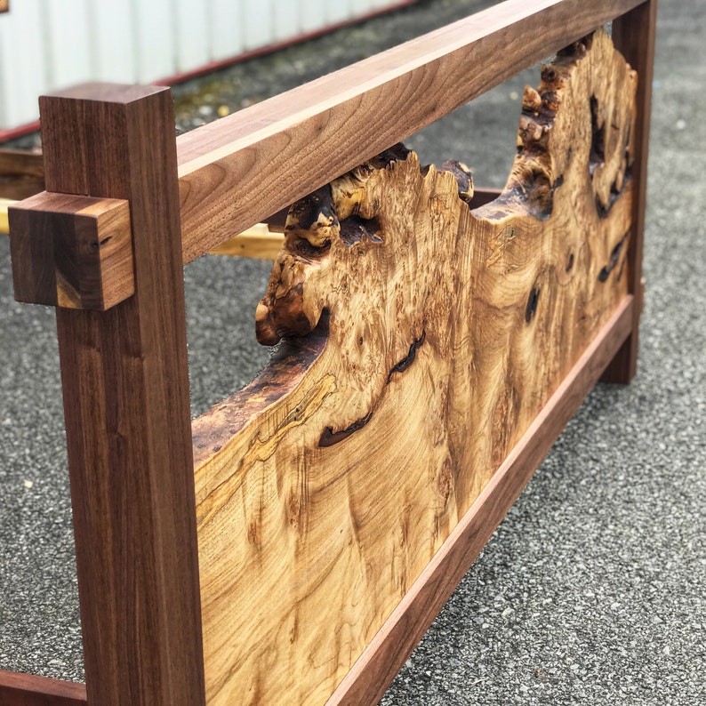 May include: A wooden bed frame with a unique headboard featuring a natural wood grain pattern. The headboard is made of a single piece of wood with a natural edge and a burl wood design. The frame is made of solid wood and has a dark brown finish.