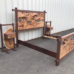 May include: A wooden bed frame with a unique headboard and footboard featuring a burl wood design. The bed frame is made of dark wood and has a simple, modern design. The headboard and footboard are both made of burl wood, which is a type of wood that has a distinctive, swirling pattern. The bed frame is also accompanied by two matching nightstands.