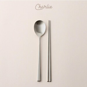 May include: A set of silver chopsticks and a spoon. The spoon has a rounded bowl and a long, slender handle. The chopsticks are thin and have a smooth finish.