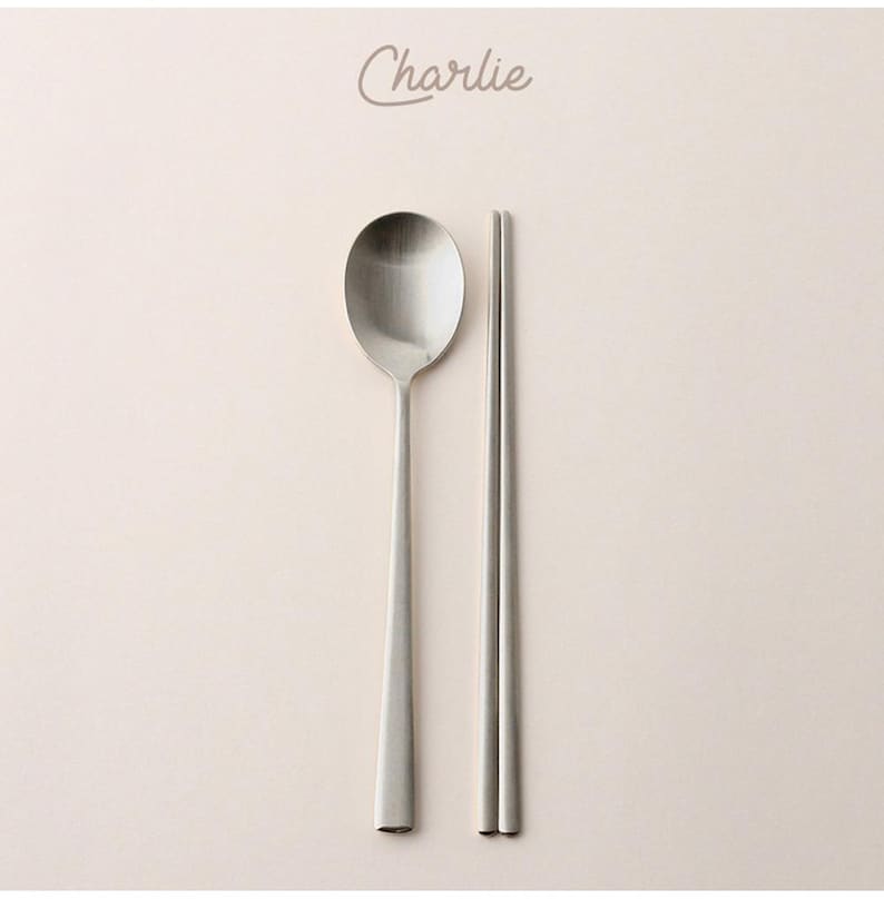 May include: A set of silver chopsticks and a spoon. The spoon has a rounded bowl and a long, slender handle. The chopsticks are thin and have a smooth finish.