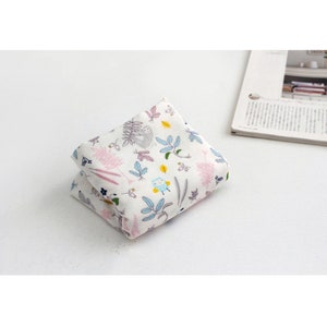 May include: A folded white fabric with a colorful pattern of sloths, owls, and plants. The fabric is folded in half and the pattern is visible on both sides.