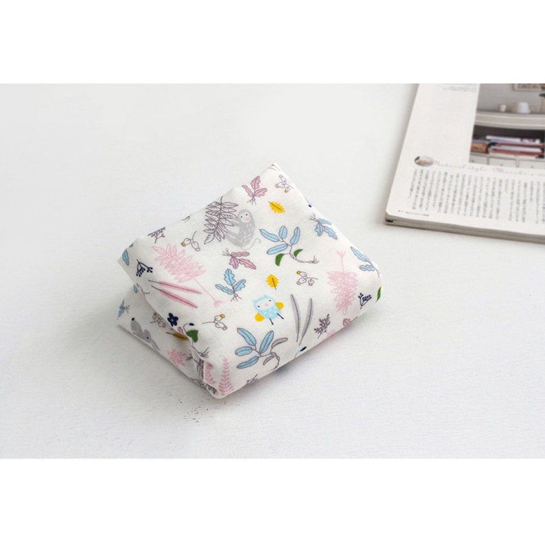 May include: A folded white fabric with a colorful pattern of sloths, owls, and plants. The fabric is folded in half and the pattern is visible on both sides.