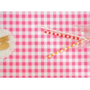 May include: Pink and white checkered tablecloth with three colorful paper straws and a glass on top. Water droplets are visible on the tablecloth.