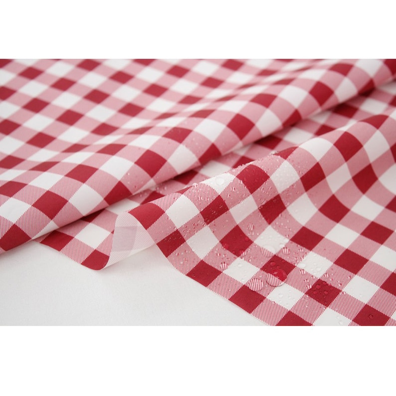 May include: Red and white checkered fabric with a water-resistant coating. The fabric is folded in half, showing the water droplets on the surface.