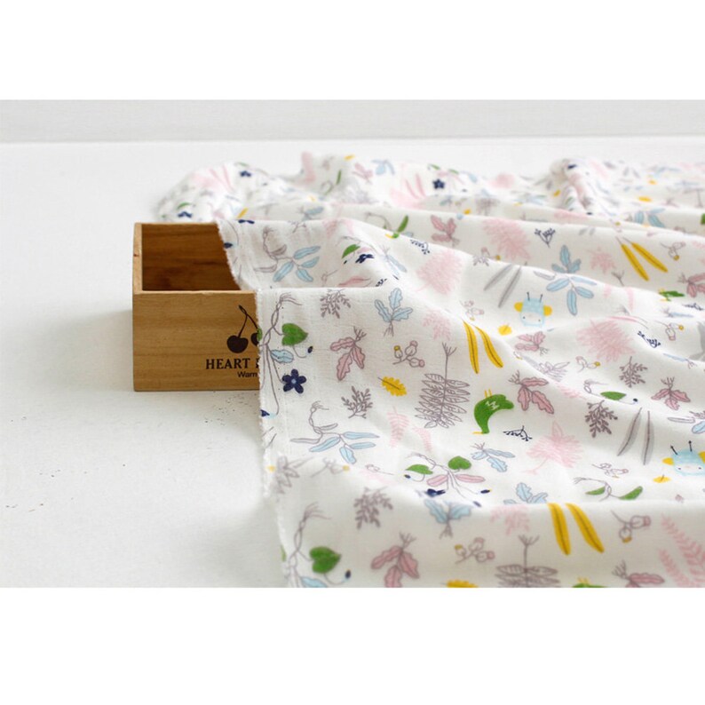 May include: White cotton fabric with a colorful floral print featuring small green, pink, and yellow flowers, leaves, and vines. The fabric has a subtle texture and a soft, lightweight feel.