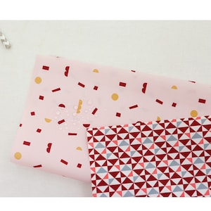 May include: Two fabric swatches with geometric patterns. The top swatch is pink with red and gold geometric shapes. The bottom swatch is red, gray, and white with a repeating triangle pattern.