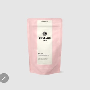 Può includere: Una bustina rosa con un'etichetta bianca su cui è scritto "OSULLOC" e "WEDDING GREEN TEA" in coreano e inglese. L'etichetta presenta anche un cerchio nero con una montagna stilizzata al suo interno.