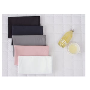May include: Five fabric swatches in different colours, stacked on top of each other. The swatches are black, navy blue, grey, pink, and white. A glass bottle with a label that says "LEM" is in the background.