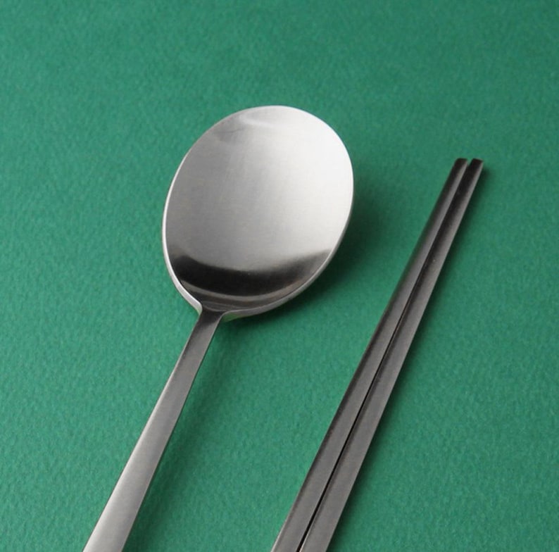 May include: A silver spoon and chopsticks on a green background.