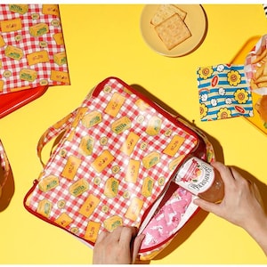 May include: A picnic-themed set featuring a red and white checkered lunch bag with a butter pattern, a red tray, and a small basket. The scene includes a burger, fries, crackers, and a jar of jam, all set against a yellow background.