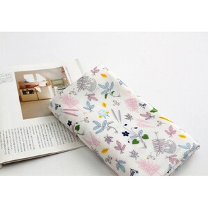 May include: White fabric with a repeating pattern of pink, green, blue, and yellow leaves, flowers, and small animals. The fabric is folded in half and lying on top of a magazine.