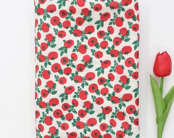 May include: A folded fabric with a repeating pattern of red poppies and green leaves on a white background. A red tulip with a green stem and leaves is on the right side of the image.