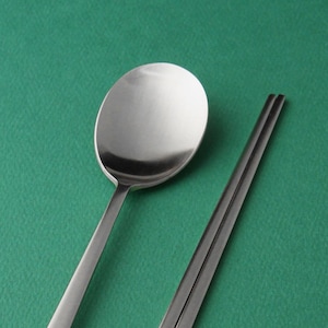 May include: A silver spoon and chopsticks on a green background.