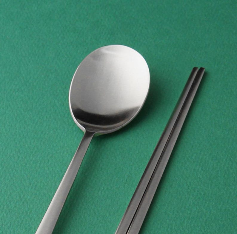 May include: A silver spoon and chopsticks on a green background.