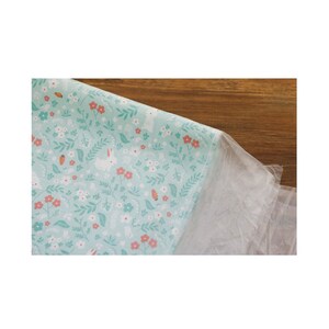 May include: A light blue fabric with a repeating pattern of white bunnies, pink flowers, and green leaves.