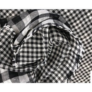 May include: Black and white gingham fabric with a frayed edge. The fabric is folded and textured.