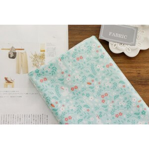May include: A light blue fabric with a white bunny rabbit and floral pattern. The fabric has a white border and the word "FABRIC" is written on a gray tag.