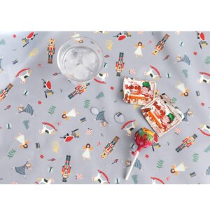 May include: A gray tablecloth with a repeating pattern of nutcrackers, ballerinas, and Christmas ornaments. There are two small red and white candy packages and a red lollipop on the tablecloth.