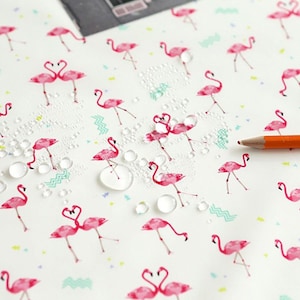 May include: White fabric with a pink flamingo pattern and colorful geometric shapes. Water droplets are scattered across the fabric. Two pencils are lying on the fabric, one orange and one yellow.
