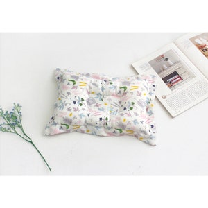 May include: A white pillow with a floral pattern in shades of pink, blue, green, and yellow. The pillow is rectangular and has a slightly raised center.