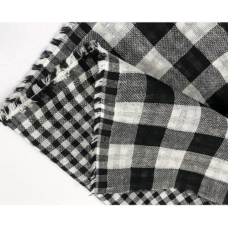 May include: Black and white checkered fabric with a frayed edge. The fabric is folded in half, revealing a second layer of checkered fabric.