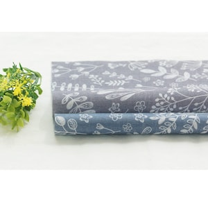 Pode incluir: Duas peças de tecido com um padrão floral branco sobre um fundo cinza e azul. O tecido está dobrado ao meio e o tecido cinza está em cima do tecido azul.
