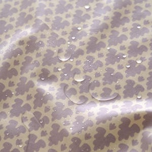 May include: Close-up of a light purple fabric with a repeating pattern of small, abstract shapes. The fabric is wet and has water droplets on it.