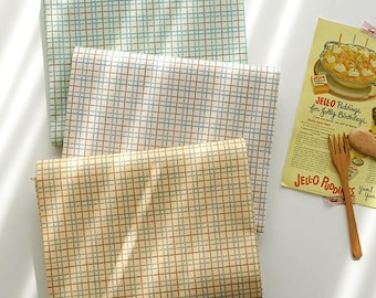 May include: Three fabric squares with a checkered pattern in shades of beige, light blue, and brown. The squares are stacked on top of each other, with the beige square on the bottom, the light blue square in the middle, and the brown square on top.
