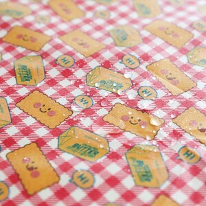 May include: A red and white checkered pattern with repeating illustrations of smiling crackers, butter cartons, and speech bubbles with the word "Hi". The design has a playful, cartoonish style.