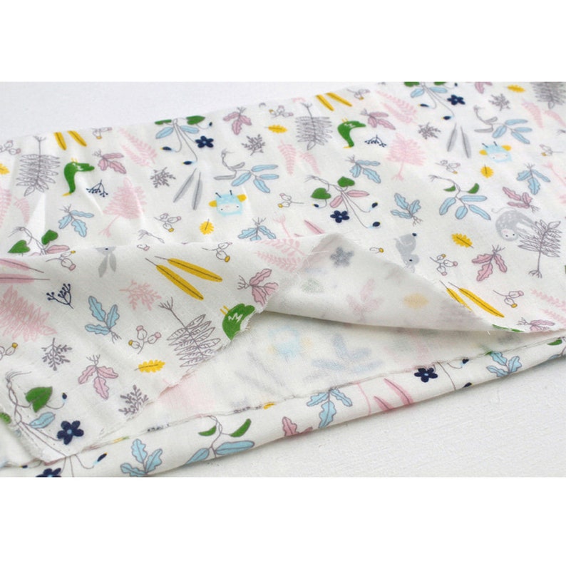 May include: White fabric with a repeating pattern of small green, blue, pink, and yellow floral and animal illustrations. The fabric is folded in half, showing the back side.