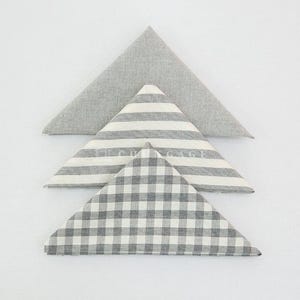 May include: Three folded cloth napkins in a triangular shape. The top napkin is solid gray, the middle one has gray and white stripes, and the bottom one has a gray and white checkered pattern. All are on a white background.