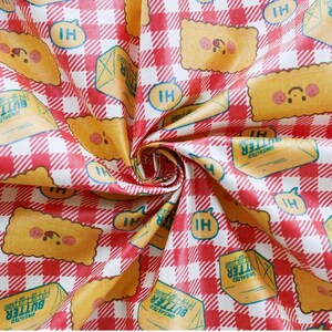 May include: Fabric with a red and white checkered pattern featuring illustrations of butter and smiling toast. The fabric also includes the text "UNSALTED BUTTER" and "HI" in speech bubbles. The design is playful and whimsical.