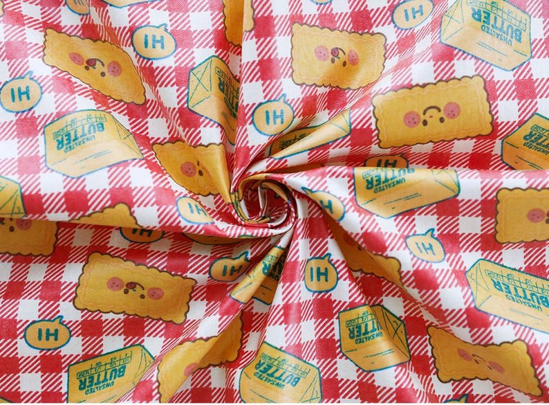 May include: Fabric with a red and white checkered pattern featuring illustrations of butter and smiling toast. The fabric also includes the text "UNSALTED BUTTER" and "HI" in speech bubbles. The design is playful and whimsical.