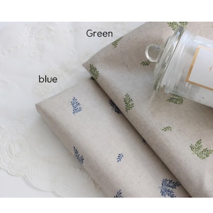 Può includere: Due rotoli di carta da regalo con un delicato motivo a foglie. Un rotolo ha foglie verdi e l'altro ha foglie blu. I rotoli sono su uno sfondo di pizzo bianco.